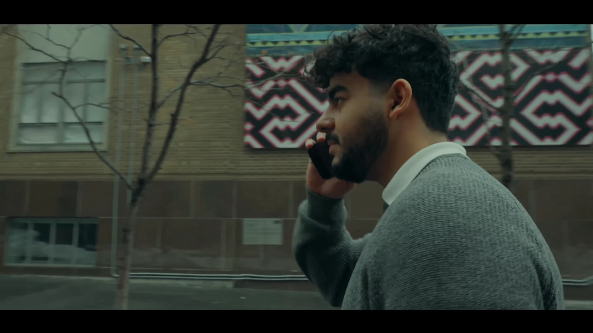 A young man walking outside while talking on the phone
